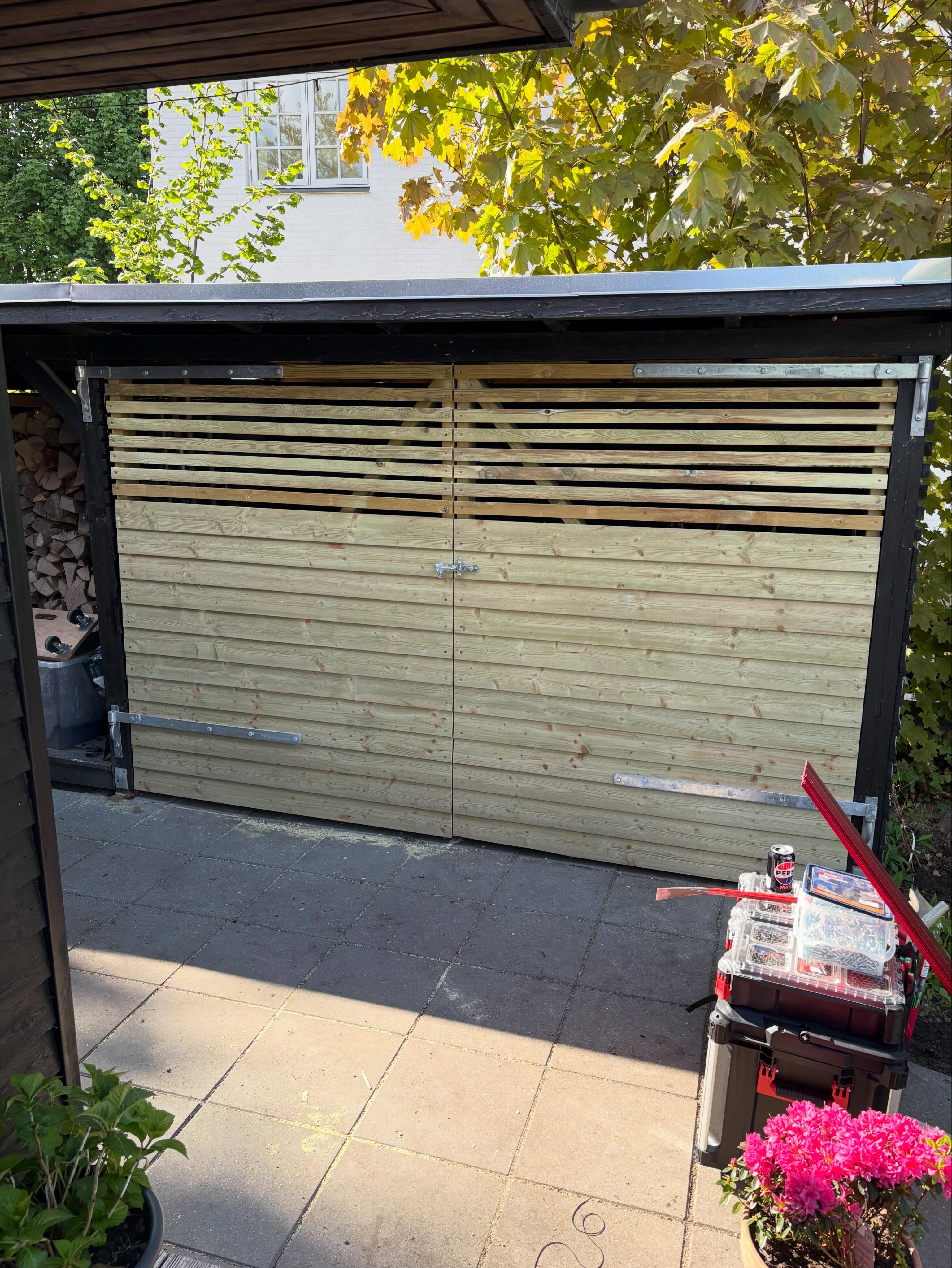 Carport med to nybyggede lyse trælameldøre og sort stolpekonstruktion