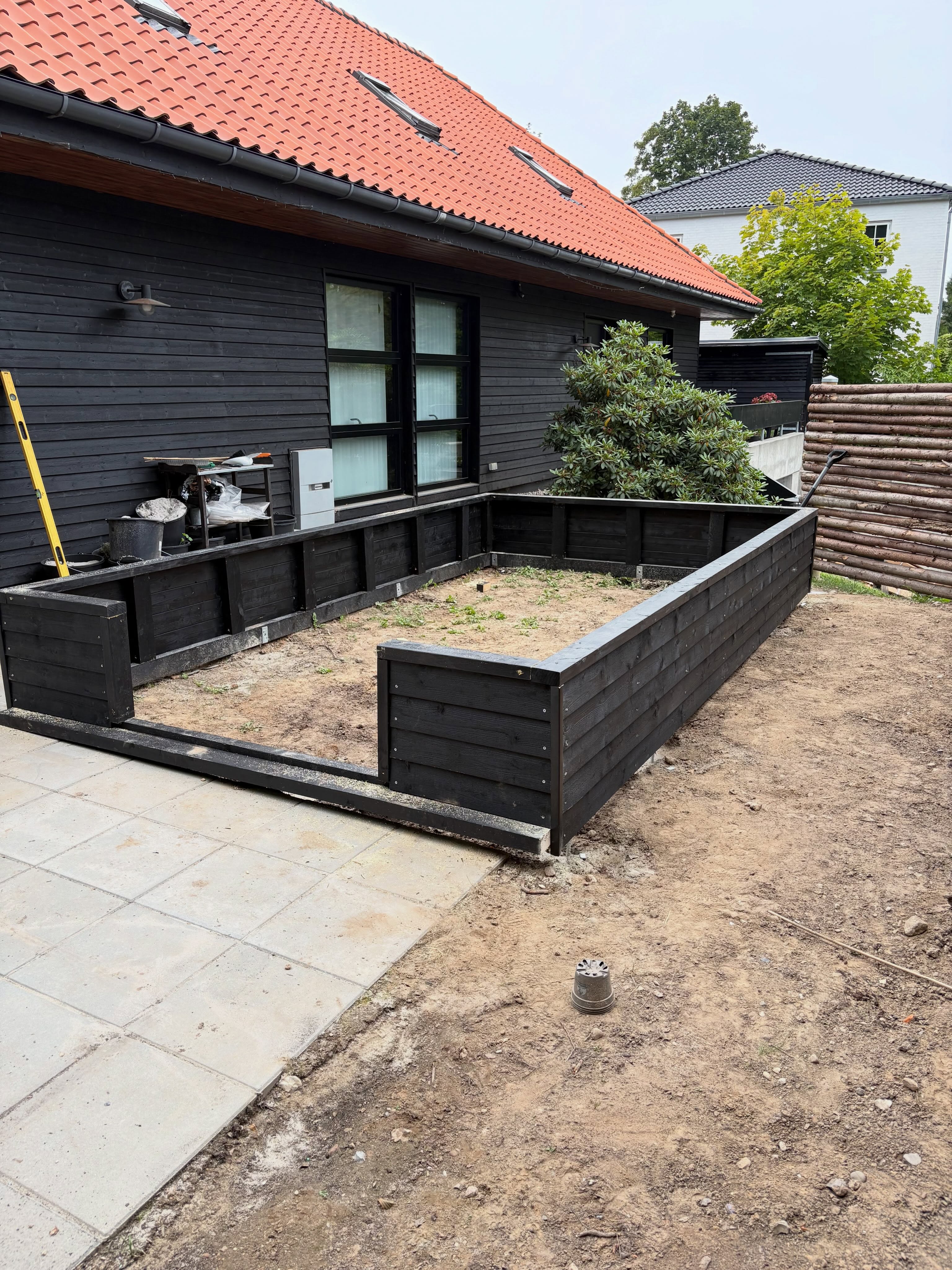 Sortbejdset terrassekonstruktion under opførelse ved et sort træhus